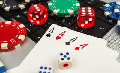 Close-up of playing cards, poker chips, and dice on a laptop keyboard.