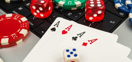 Close-up of playing cards, poker chips, and dice on a laptop keyboard.