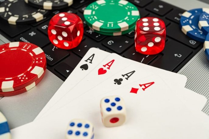 Close-up of playing cards, poker chips, and dice on a laptop keyboard.